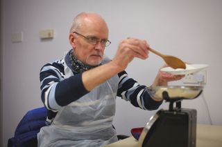 A photo of a man cooking in a kitchen. He is concentrating on weighing out ingredients on a set of kitchen scales.