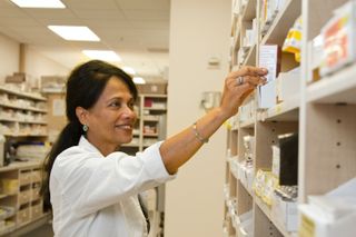 A photo of a pharmacist in a pharmacy. She is smiling.